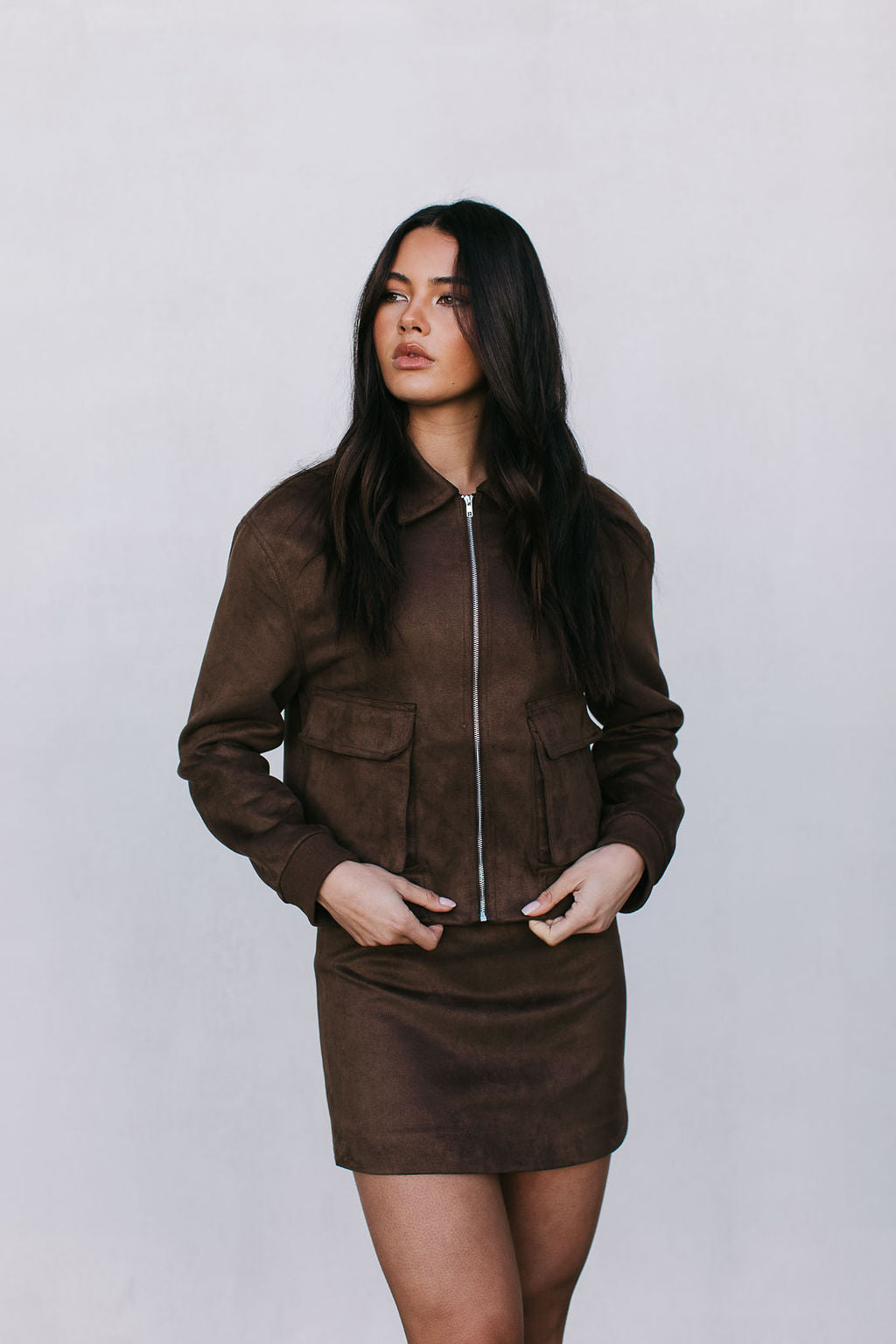 Woman wearing a brown jacket and skirt set against a plain background