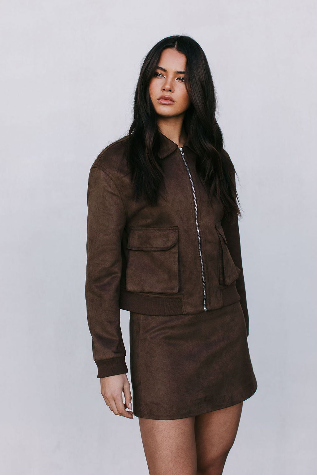 Woman wearing a brown suede jacket and skirt on a plain background
