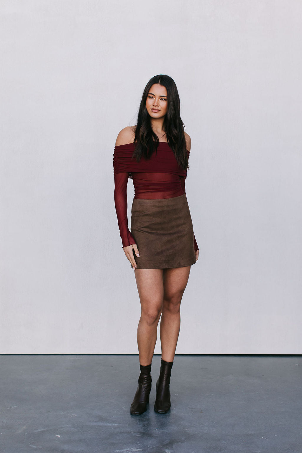 Woman wearing a burgundy off-shoulder top and brown skirt against a white background
