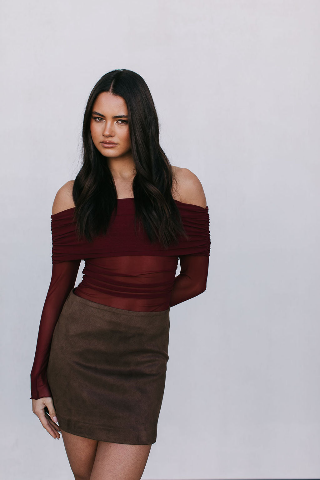 Woman wearing a burgundy off-shoulder top and brown skirt against a white background