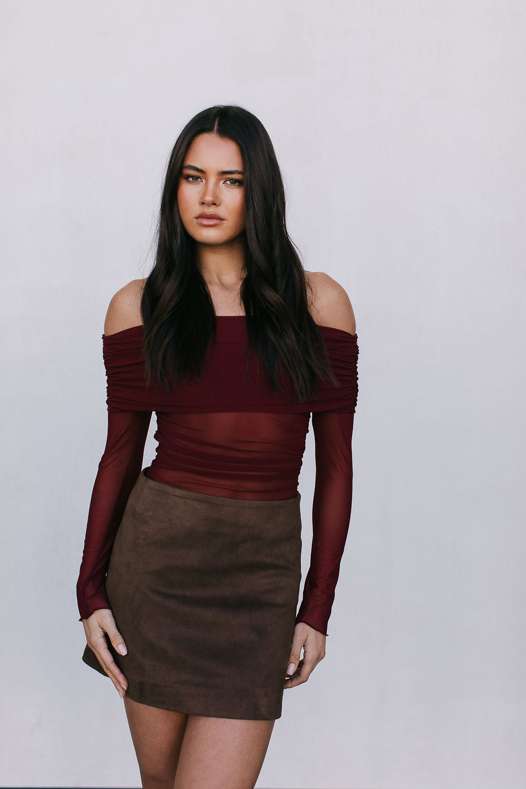 Woman wearing a burgundy off-shoulder top and brown skirt against a white background