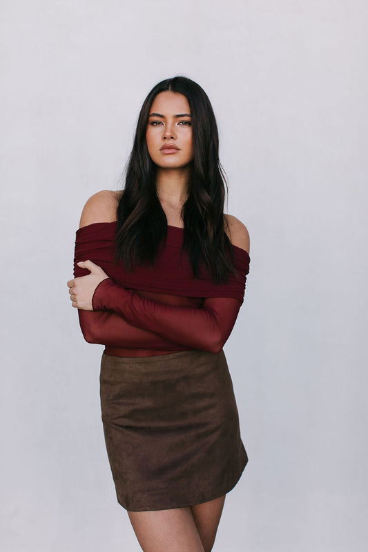 Woman wearing a burgundy off-shoulder top and brown skirt against a plain background