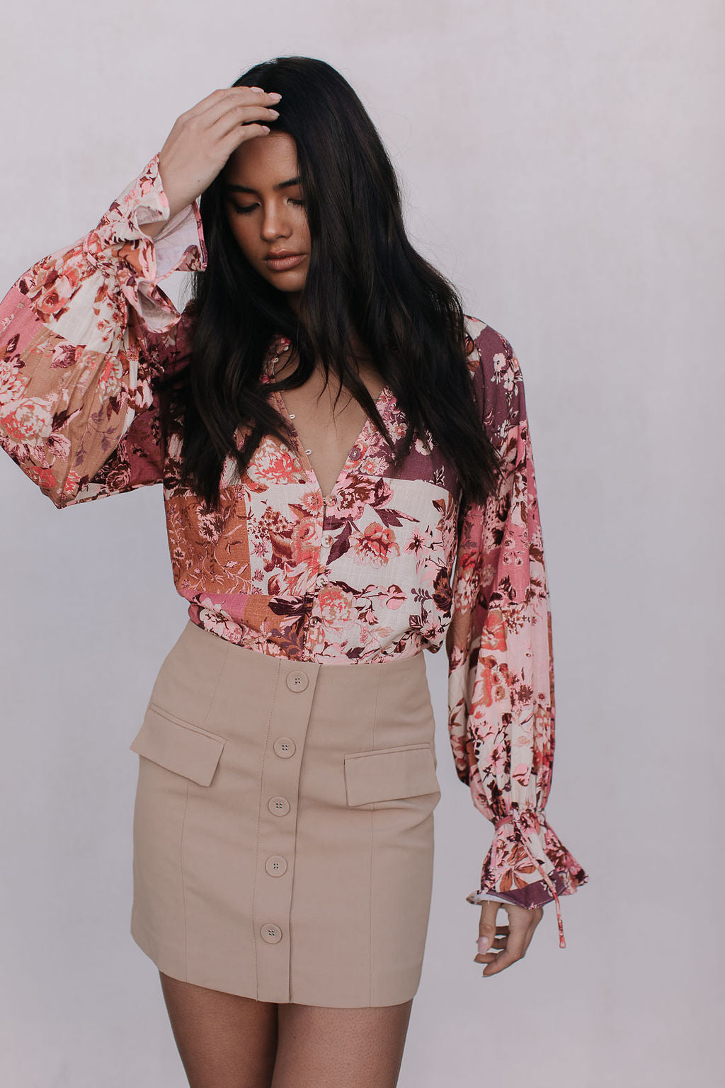 Woman wearing a floral blouse and beige skirt against a white background