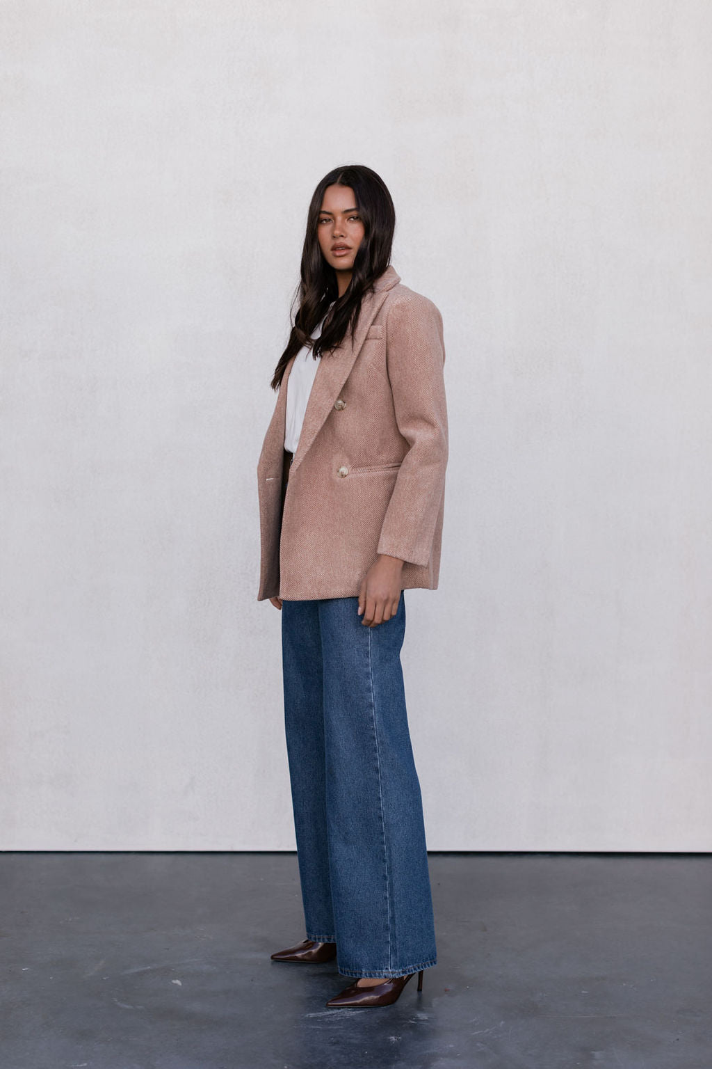 Woman wearing a beige blazer and blue jeans against a white background