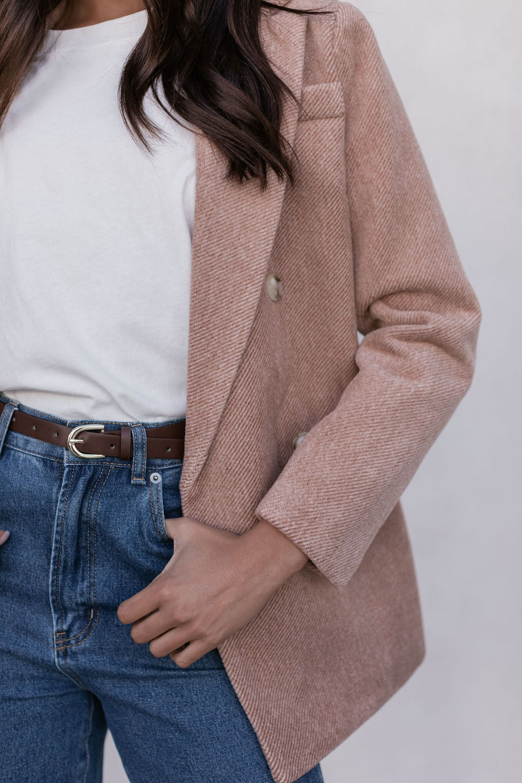 Person wearing a beige blazer over a white top and blue jeans on a plain background