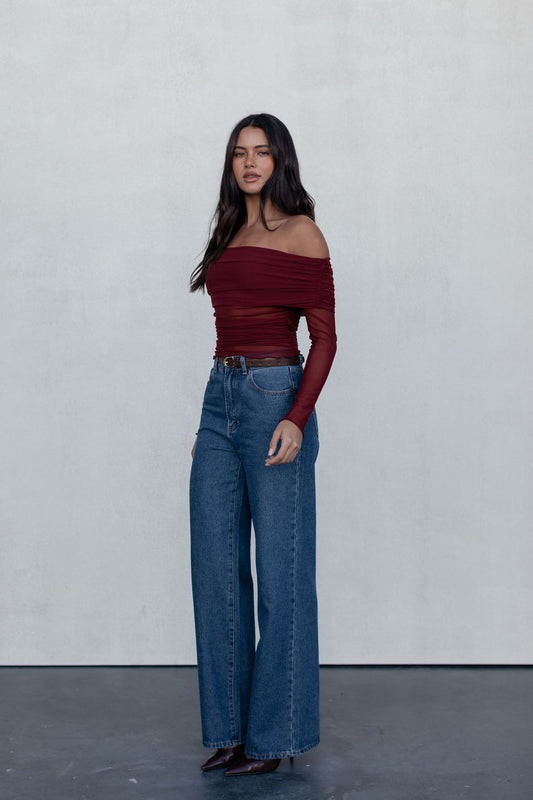 Woman wearing a burgundy off-shoulder top and blue jeans against a white background