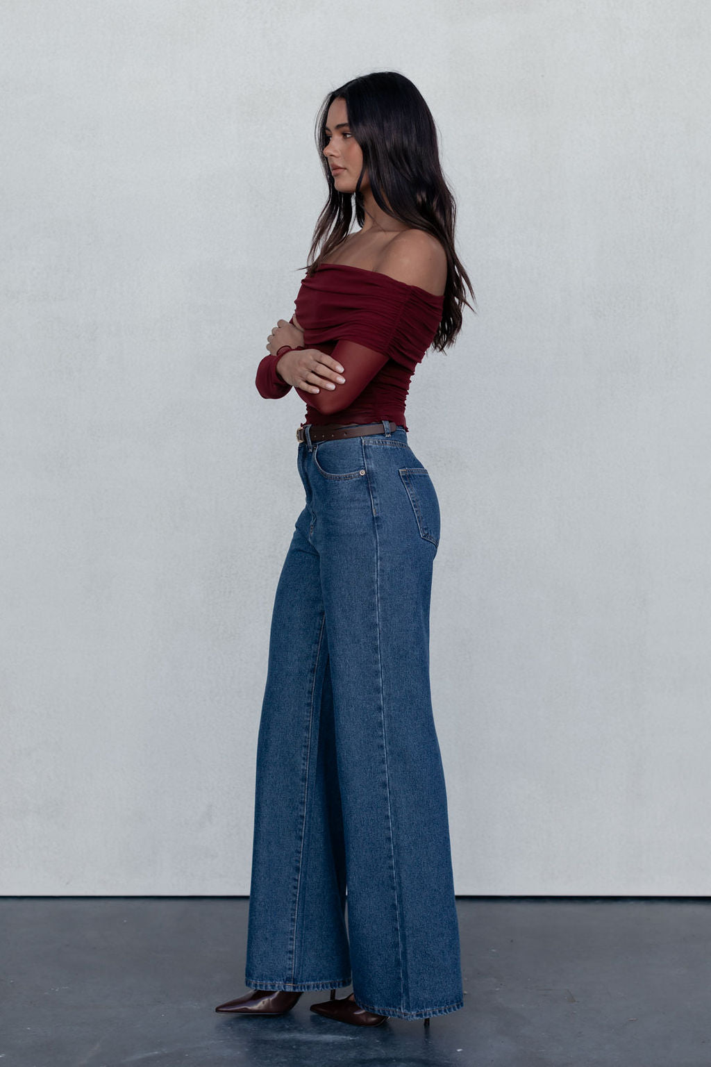Woman wearing a burgundy top and blue jeans against a plain background