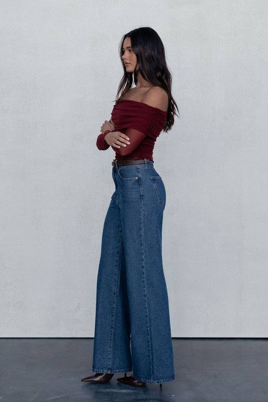 Woman wearing a burgundy top and blue jeans against a plain background