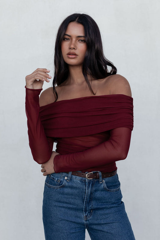 Woman wearing a burgundy off-shoulder top and blue jeans against a white background