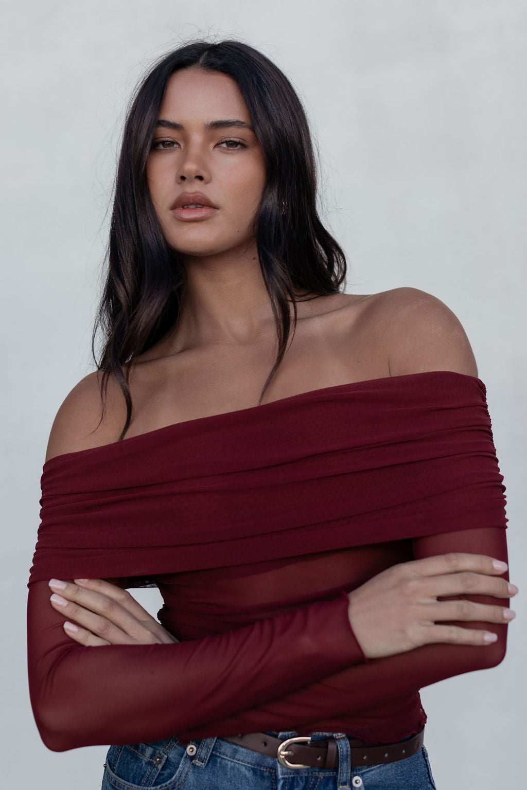 Woman wearing a burgundy off-shoulder top against a plain background
