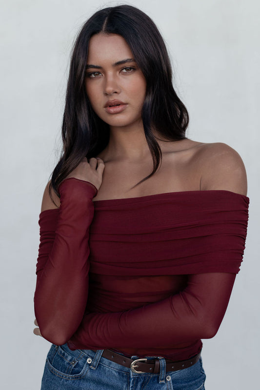 Woman wearing a burgundy off-shoulder top and blue jeans against a white background