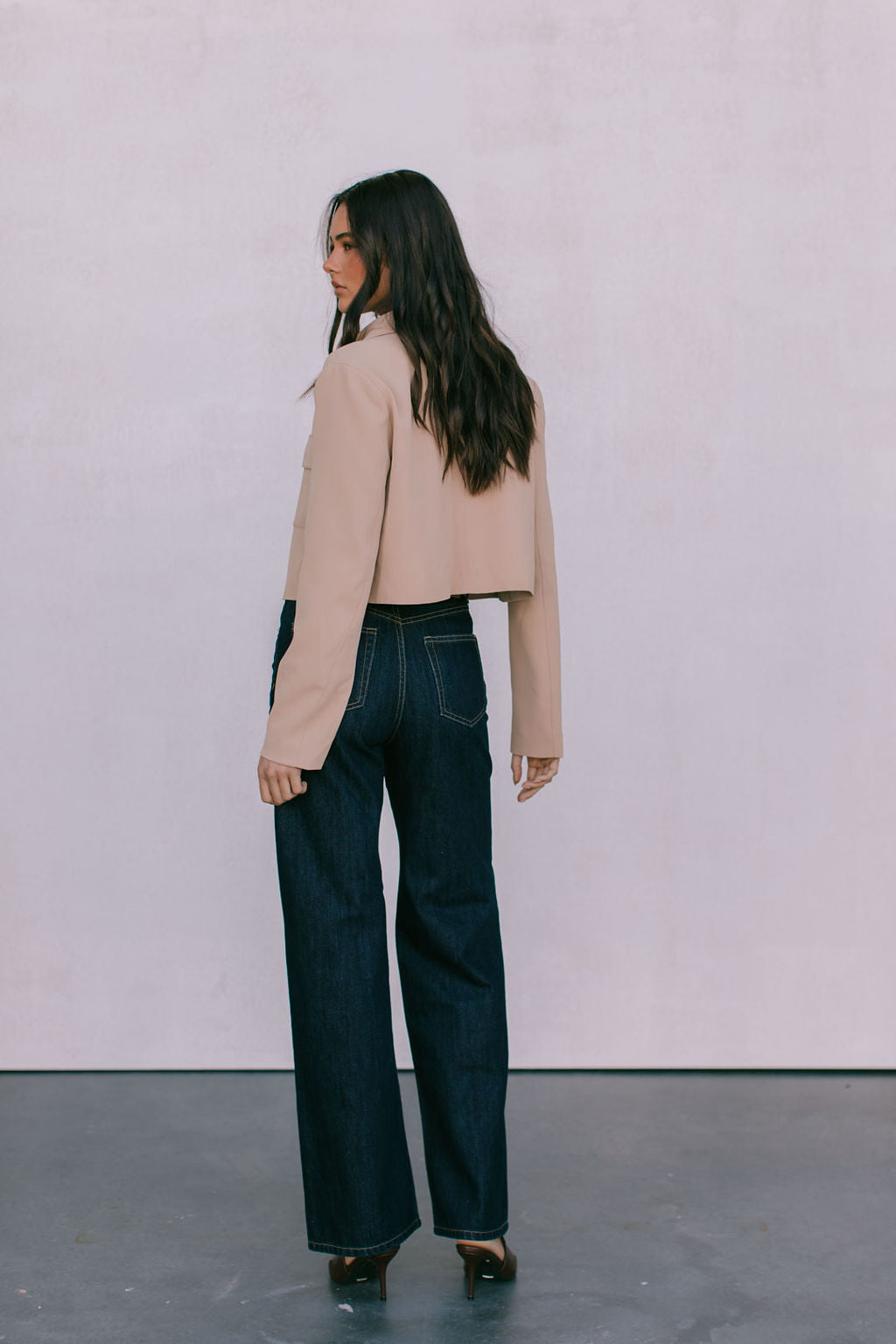 Woman wearing a beige jacket and dark jeans against a plain background