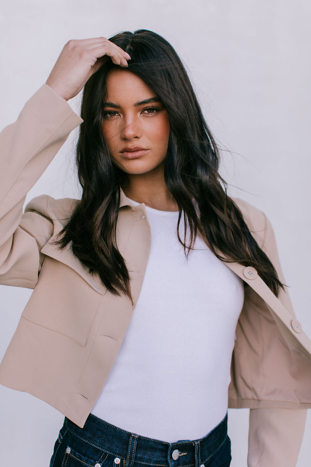 Woman wearing a beige blazer over a white top with a plain background