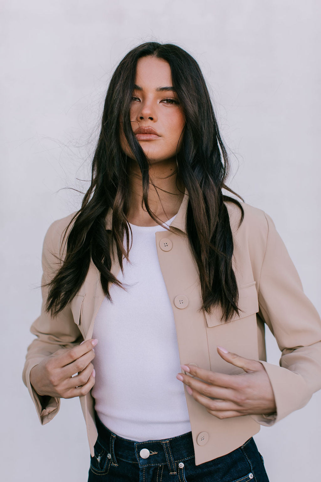Woman wearing a beige jacket over a white shirt with a plain background