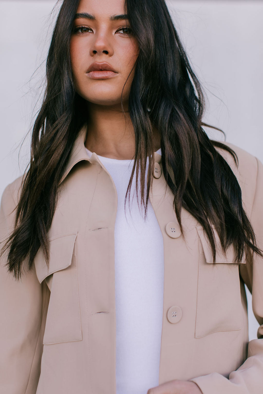 Woman wearing a beige jacket over a white shirt against a neutral background