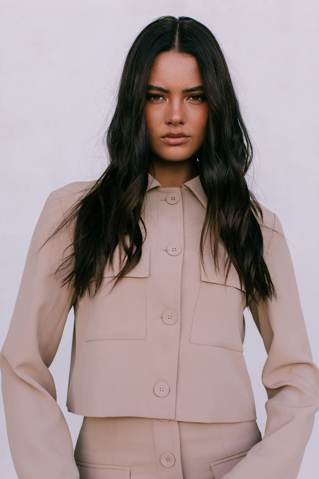 Woman wearing a beige suit against a plain background