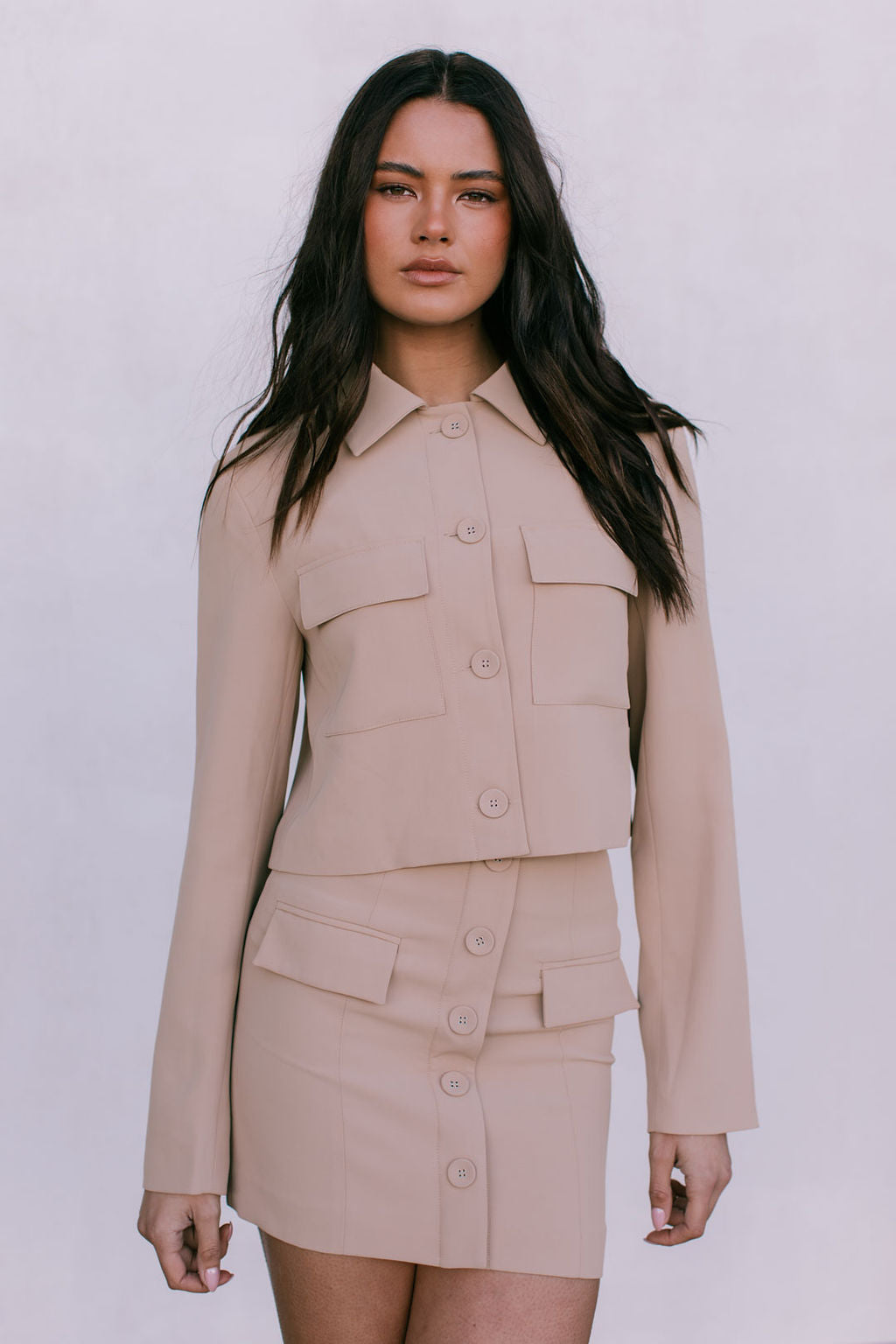 Woman wearing a beige two-piece suit against a white background