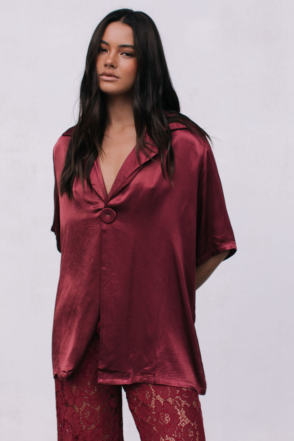 Woman wearing a burgundy satin top with lace pants on a white background