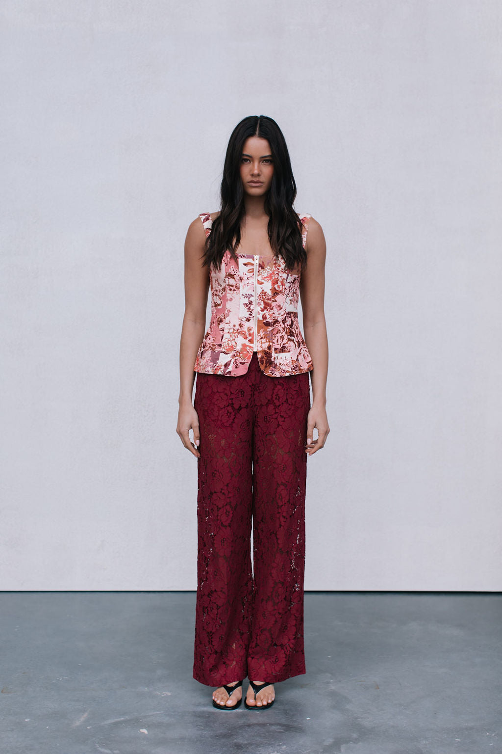 Woman wearing a floral top and red lace pants against a plain background