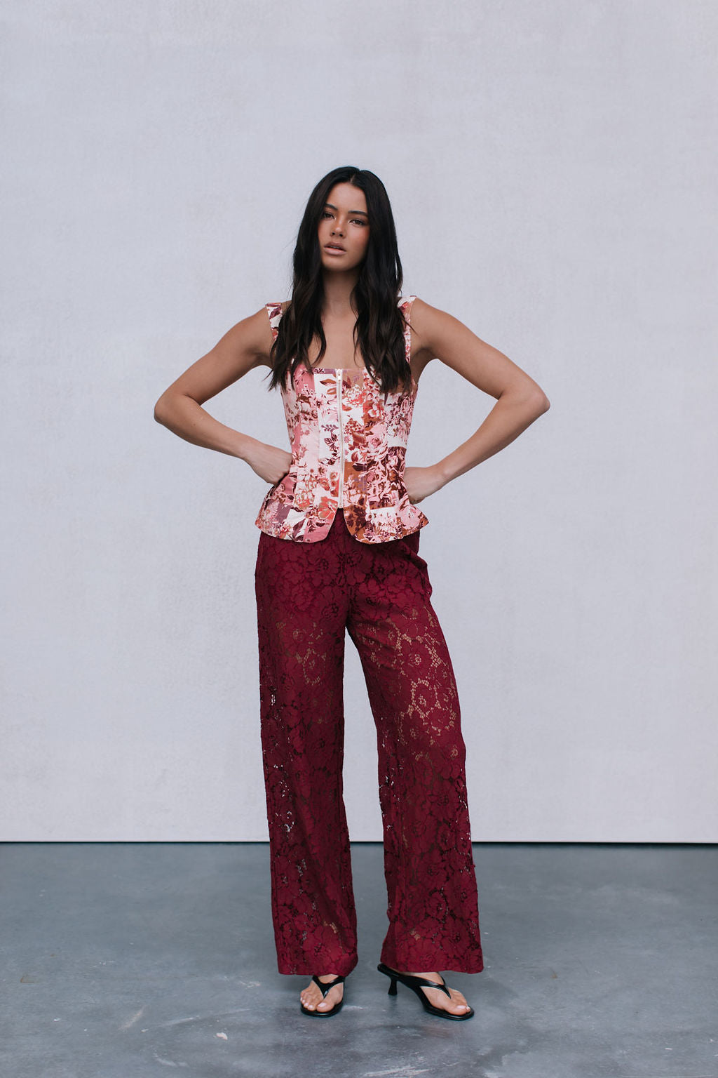 Woman wearing a floral top and red lace pants against a plain background