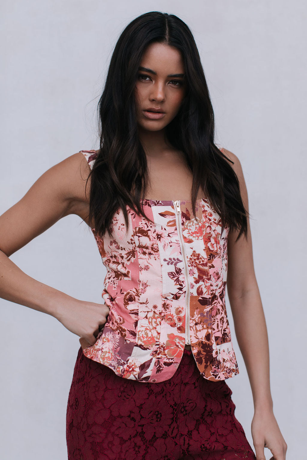 Woman wearing a floral top and maroon skirt against a plain background