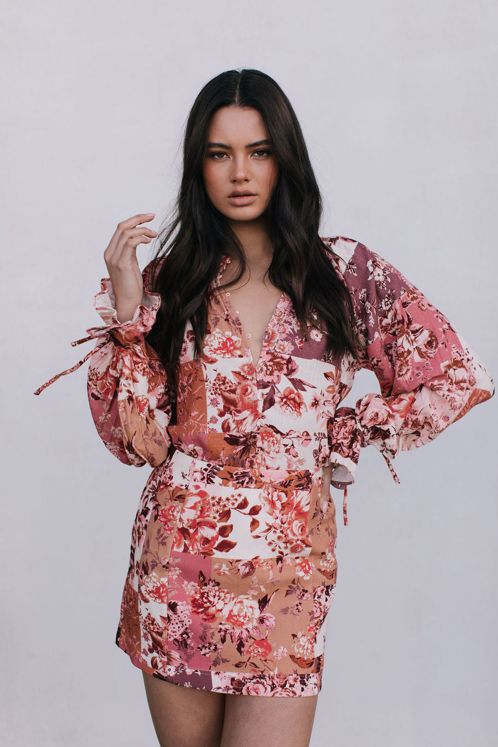 Woman wearing a floral blouse and mini skirt on a plain background
