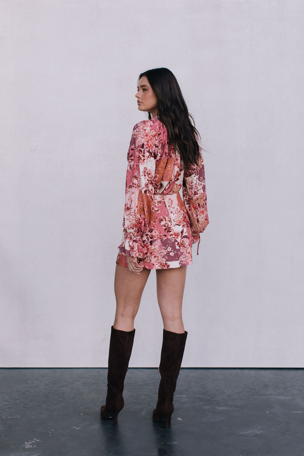 Woman wearing a floral dress and knee-high boots against a plain background
