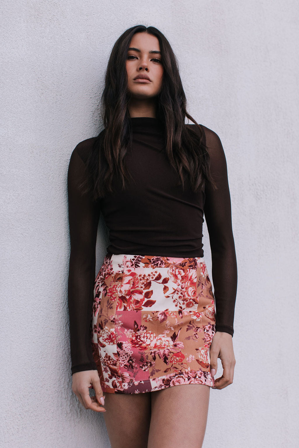 Woman wearing a brown top and floral skirt against a plain background