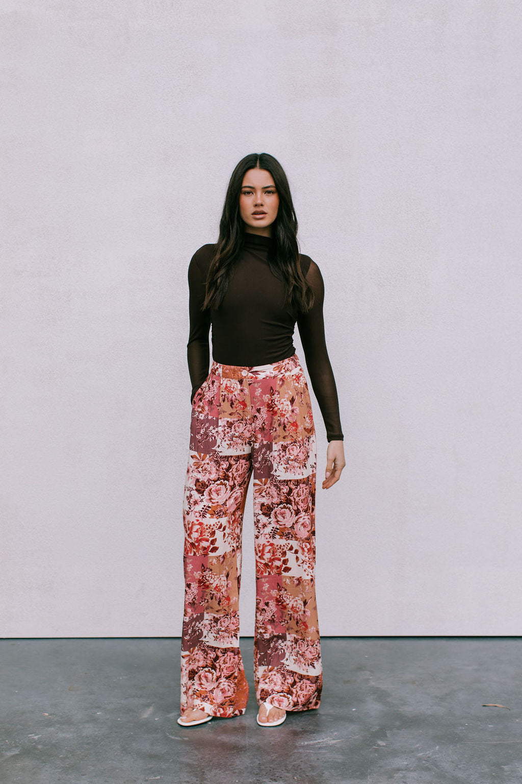 Woman wearing a brown top and floral pants against a plain background
