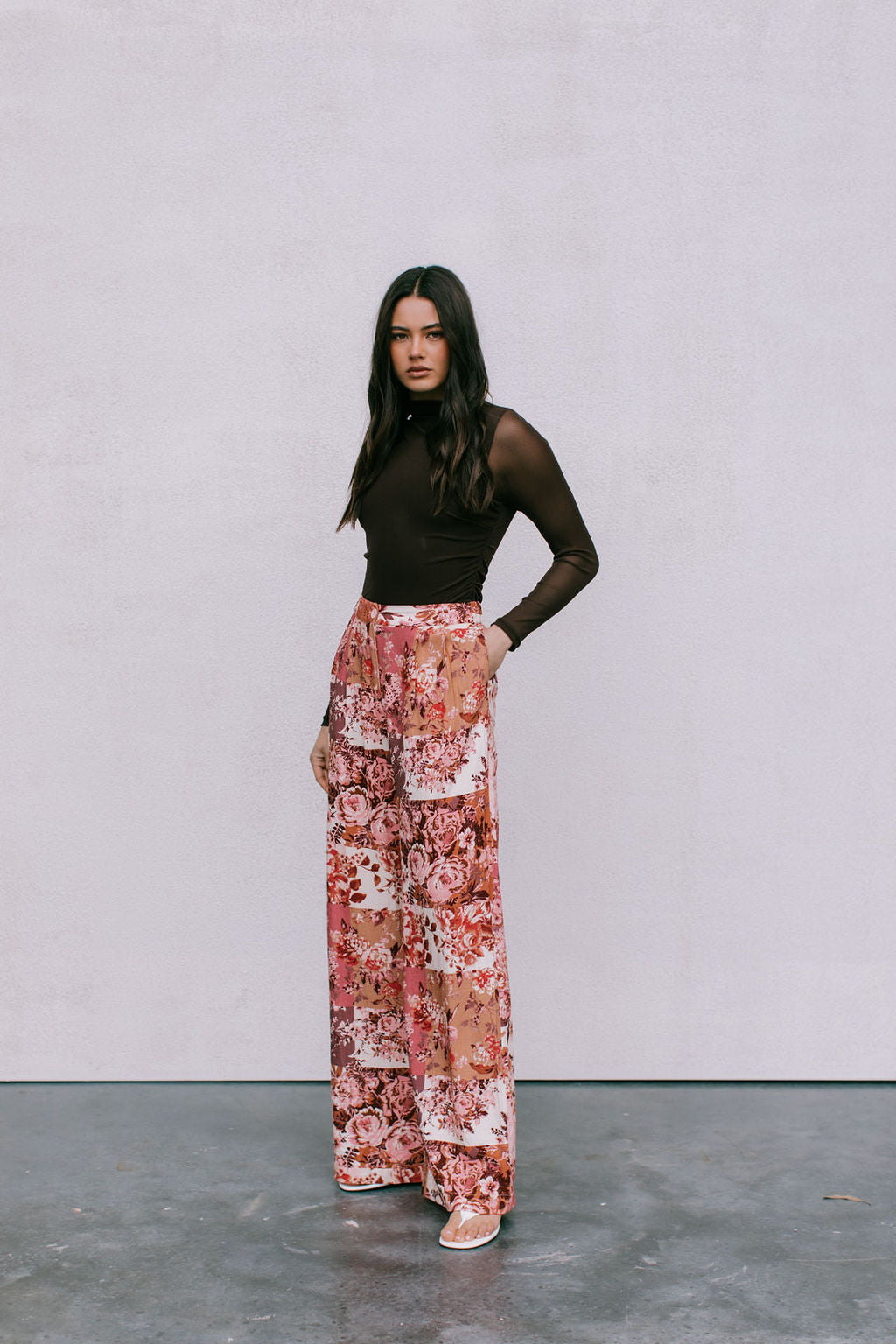 Woman wearing a brown top and floral pants against a plain background
