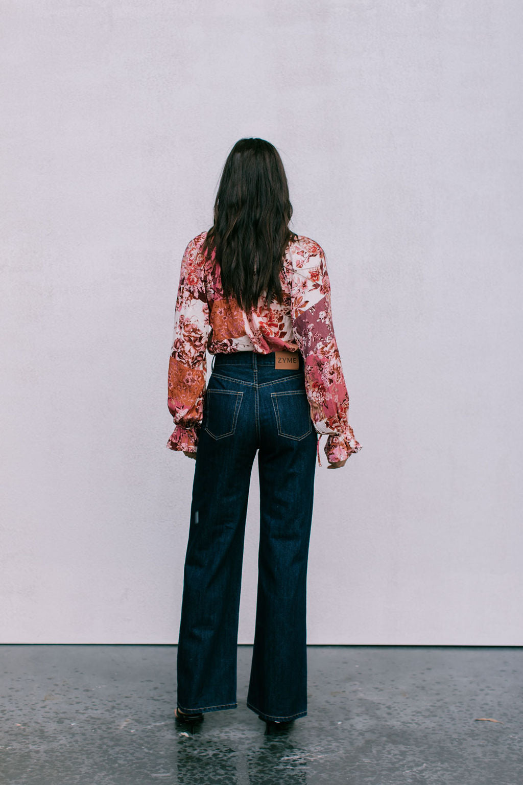 Person wearing a floral blouse and dark jeans standing against a plain background