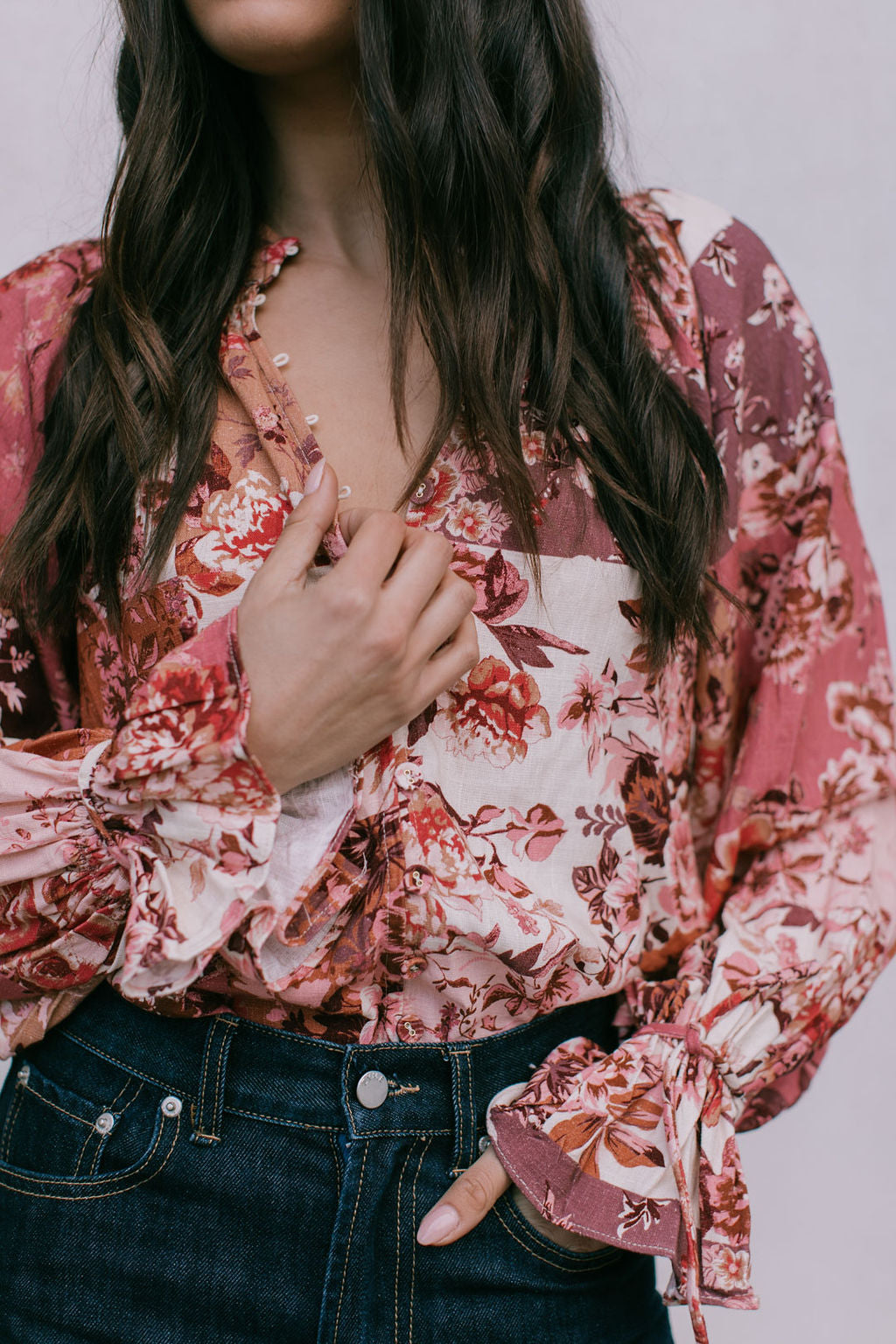 Person wearing a floral blouse with long sleeves and dark jeans on a plain background