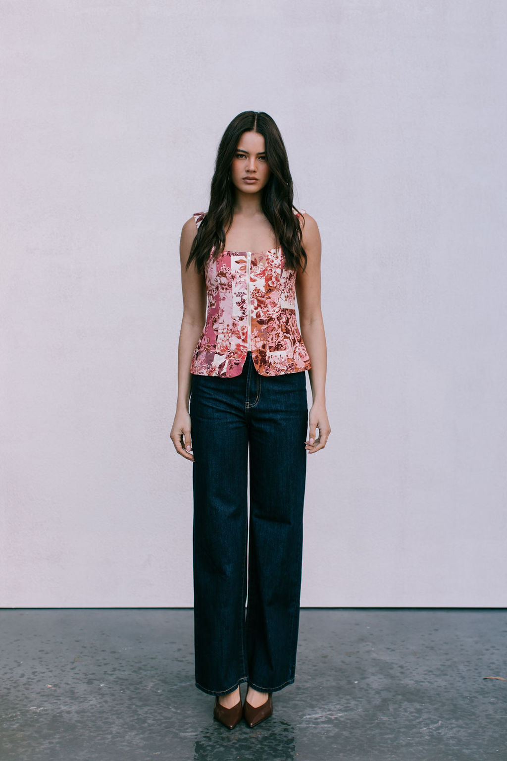 Woman wearing a floral top and dark jeans against a plain background