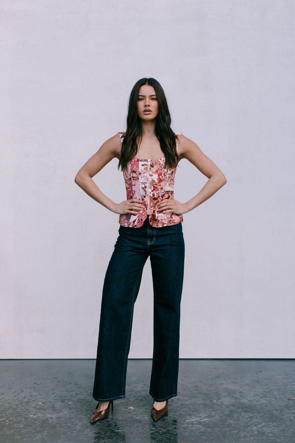 Woman wearing a floral top and dark jeans against a plain background