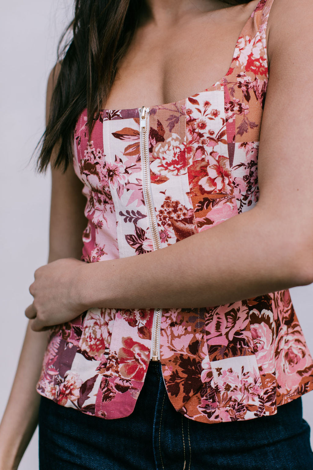 Woman wearing a floral sleeveless top with a zipper detail against a neutral background