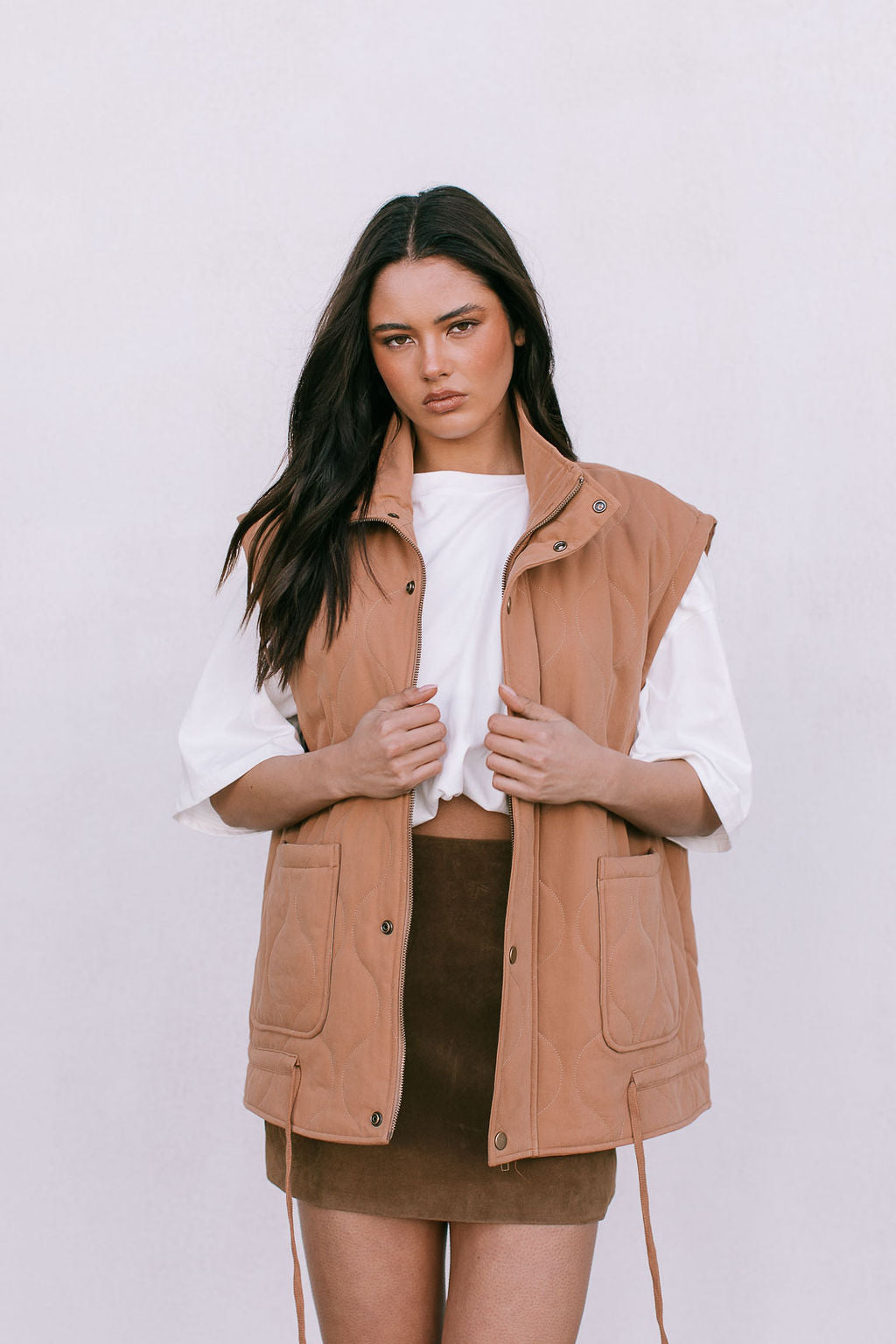 Woman wearing a brown vest over a white shirt and brown skirt on a white background