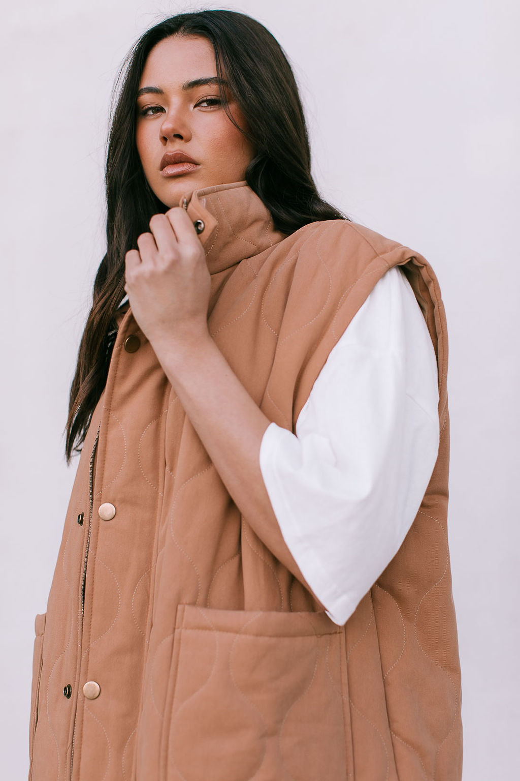Woman wearing a brown puffer vest over a white shirt against a white background