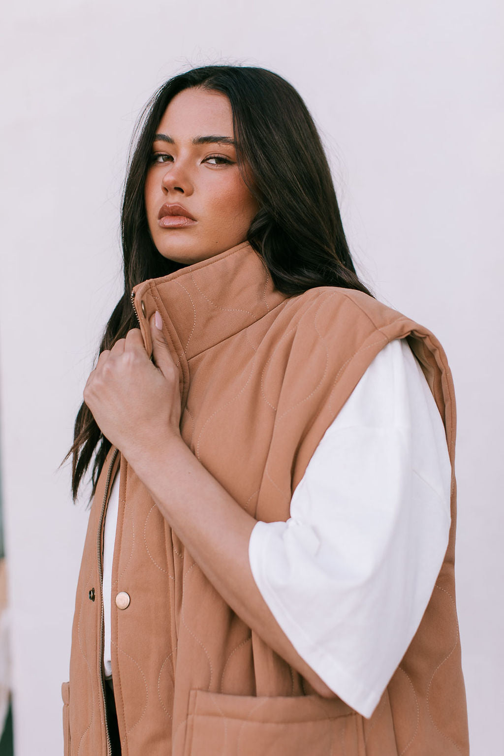 Woman wearing a brown vest over a white shirt against a white background