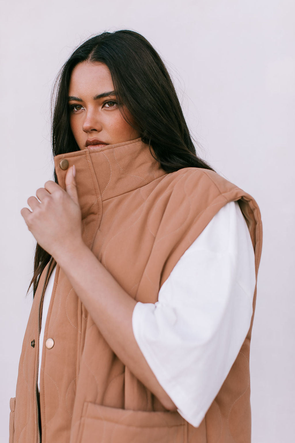 Woman wearing a brown puffer vest with white sleeves against a plain background