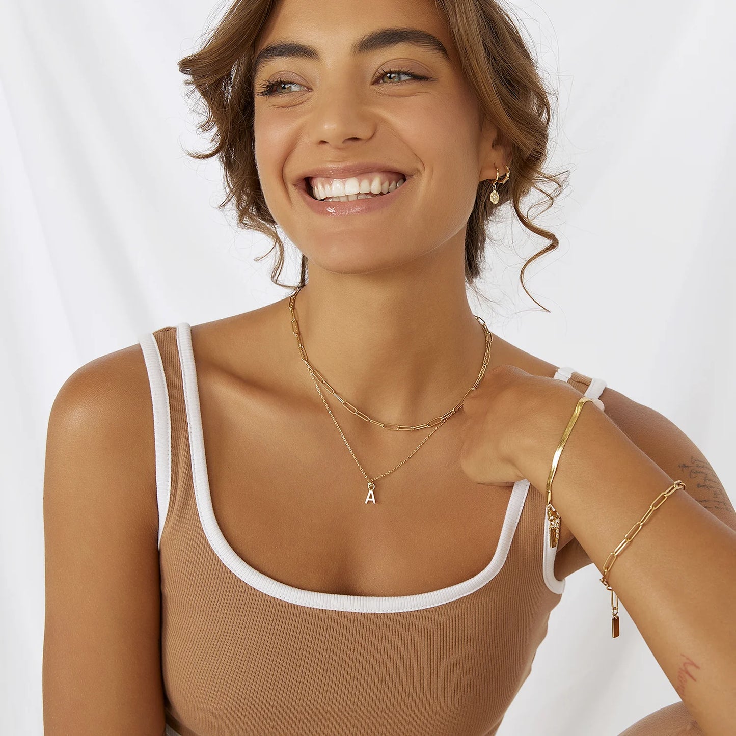 Photo of a woman styled in gold jewelery and smiling wearing a neutral top.