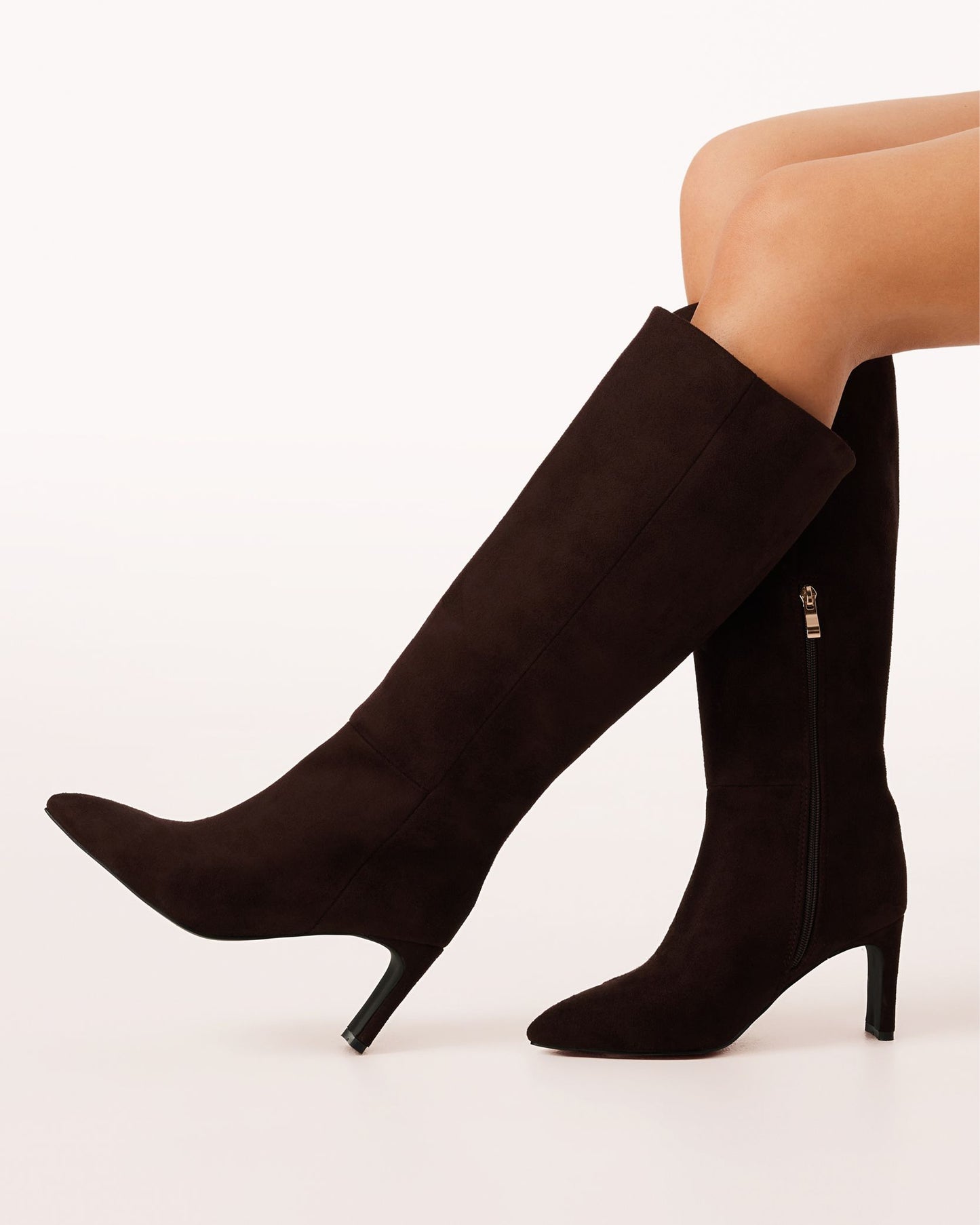 A chocolate brown suede knee-high boot with a pointed toe and high heel.