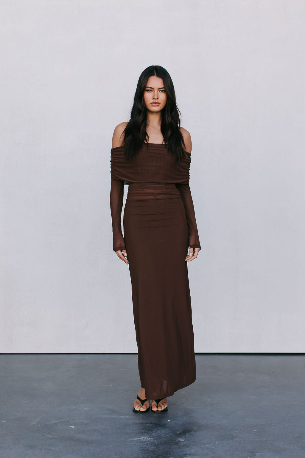 Woman wearing a brown off-shoulder dress against a plain background