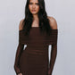 Woman wearing a brown off-shoulder dress against a plain background