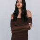 Woman wearing a brown off-shoulder dress with sheer sleeves against a plain background