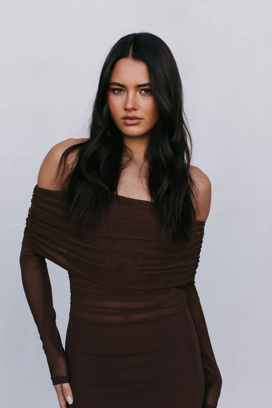 Woman wearing a brown off-shoulder dress against a plain background