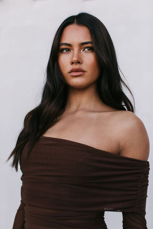 Woman wearing a brown off-shoulder top against a plain background