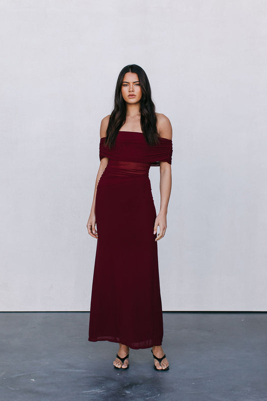 Woman wearing a burgundy off-shoulder dress against a plain background