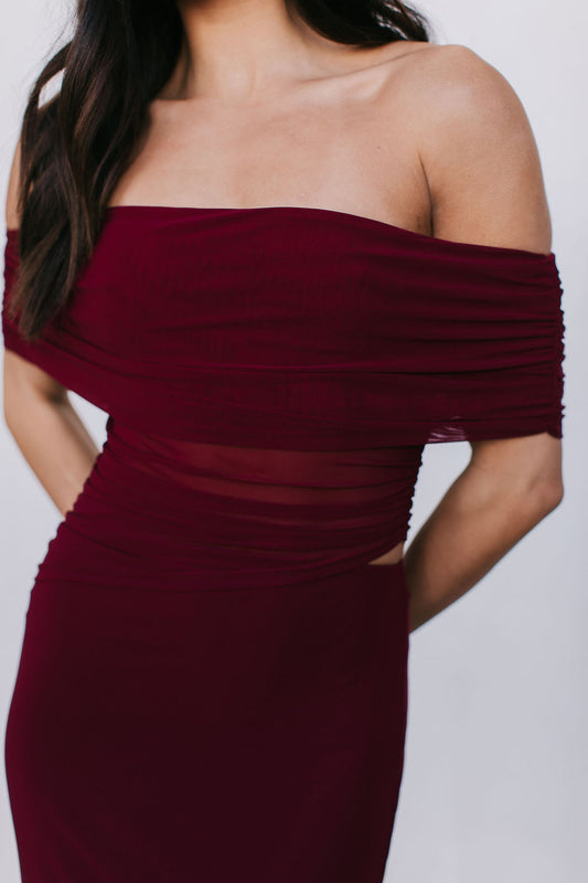 Burgundy off-shoulder dress worn by a person on a plain background
