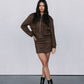 Woman wearing a brown jacket and skirt set with black boots on a plain background