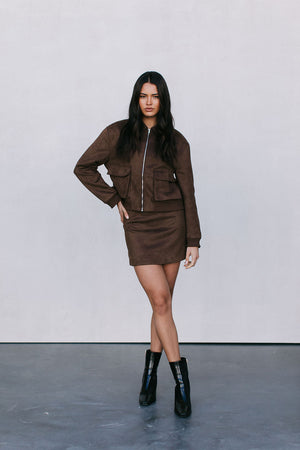 Woman wearing a brown jacket and skirt set with black boots on a plain background